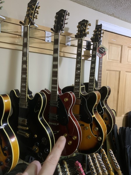 Me pointing to a semi-hollowbody guitar at a guitar shop