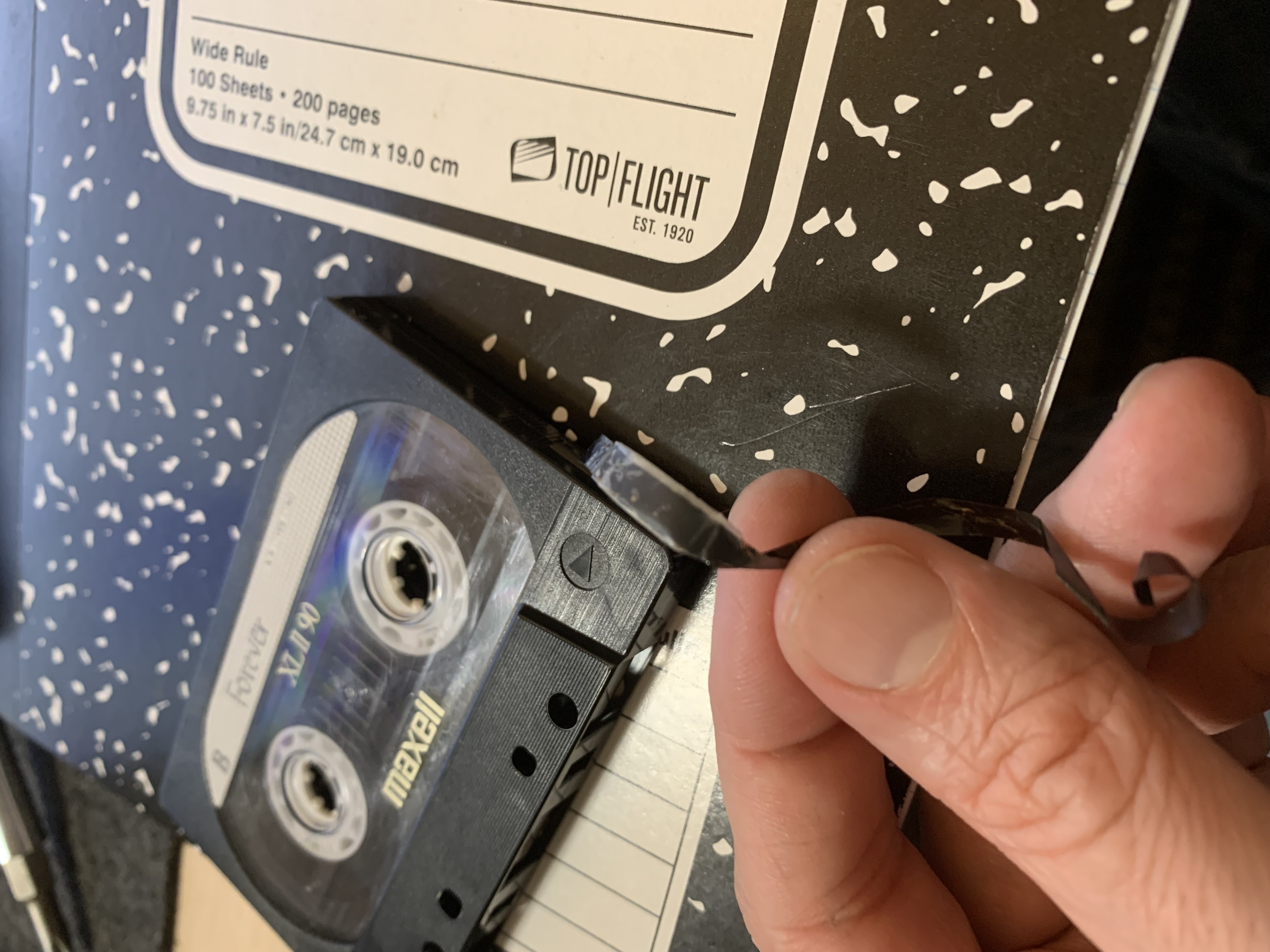A hand holding a piece of broken tape next to a tape and notebook